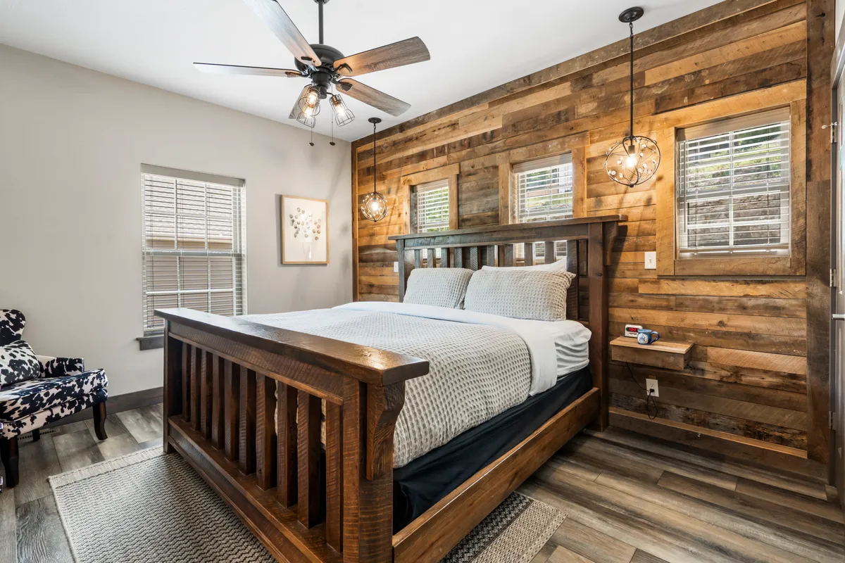 A restful king suite with a wooden bed frame, textured accent wall, pendant lights, and a large window allowing natural sunlight. The ambiance is serene, with soft bedding and subtle decor touches.