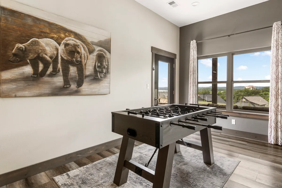 A playful downstairs living area featuring a foosball table, bear-themed wall art, and large windows letting in plenty of natural light. The space radiates a relaxed and energetic vibe, ideal for games and kids’ activities.