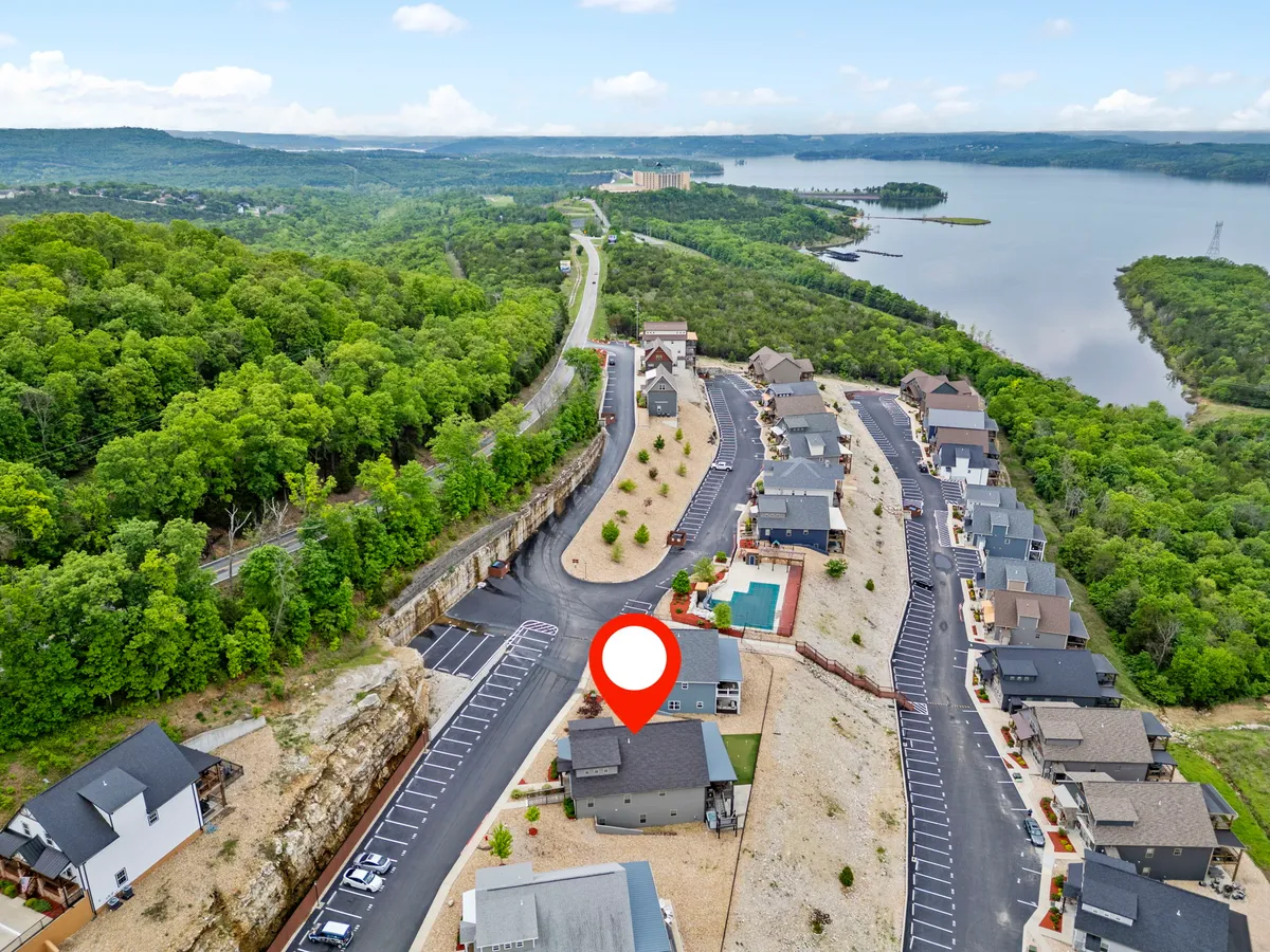 A picturesque exterior view featuring residential buildings nestled among lush greenery, a winding road, and a serene lake in the distance. The scene invites leisurely walks and a sense of peaceful community living.