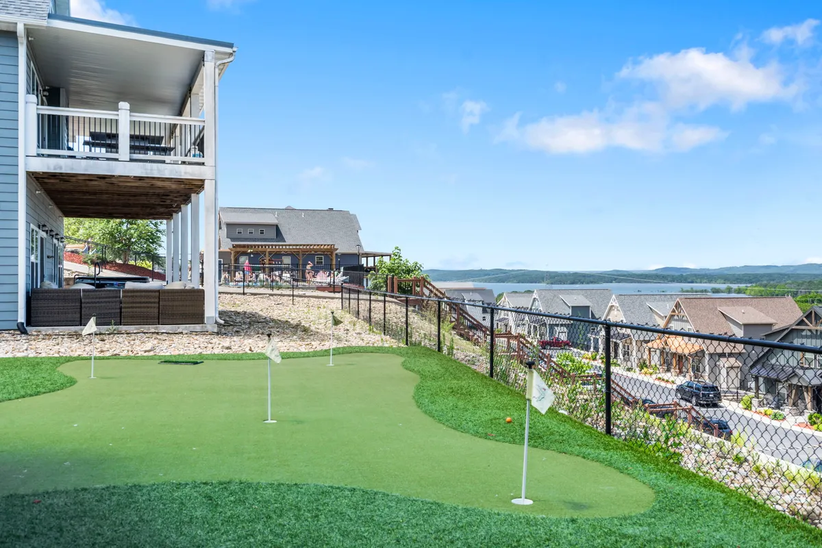 This exterior scene showcases the Lodge’s private golf putting green with golf flags set against a stunning lake view and surrounding residential homes. The green is bathed in sunlight, offering a playful and serene backdrop for guests practicing their short game or gathering outdoors.