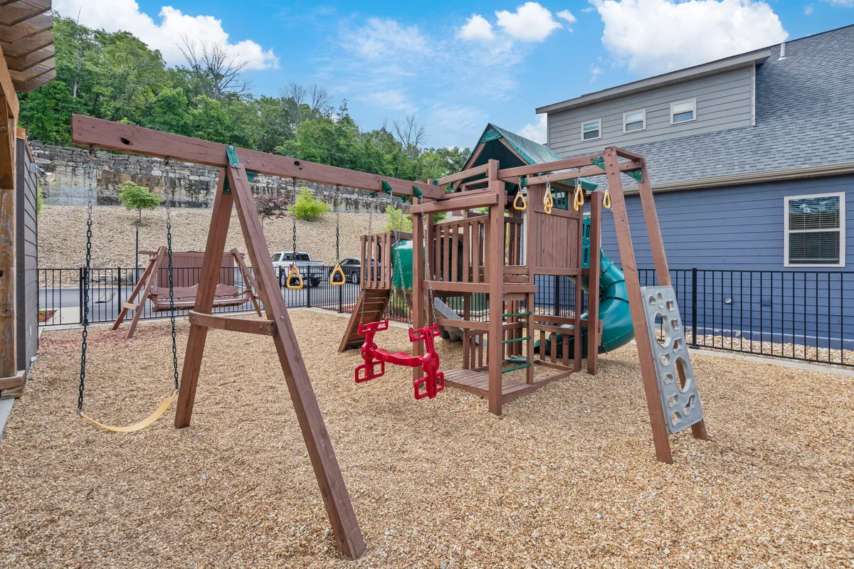 A cheerful playground area with modern equipment, swings, and a sandbox, surrounded by greenery. Children are seen playing energetically while adults supervise and enjoy the pleasant outdoor setting.
