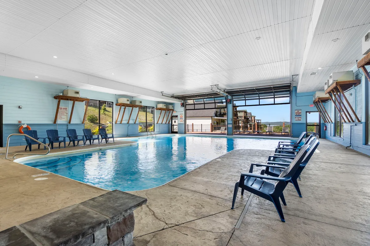 A bright indoor swimming pool featuring reclining chairs along the poolside and large windows letting in natural light. Several people are seen swimming, relaxing, and socializing by the water, evoking a tranquil and leisurely mood.