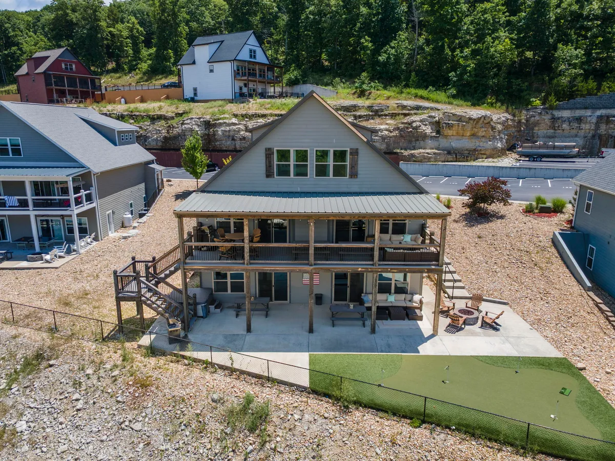 This exterior image showcases the two-story Lakeview Green Lodge with its spacious front deck, inviting patio seating, and natural landscape setting. The view captures the lodge's communal outdoor spaces perfect for gatherings, relaxation, and team-building activities.