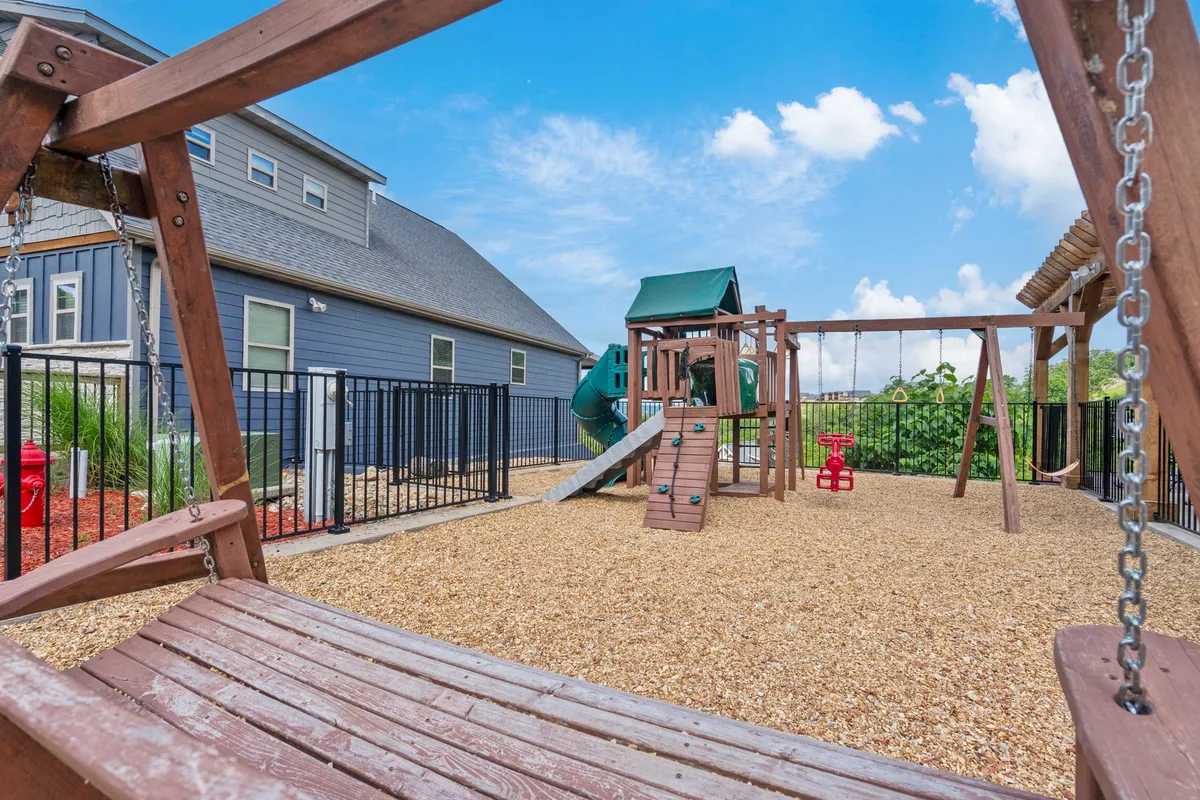 A lively playground scene with swing sets and sandbox, surrounded by green space, where children are seen playing and families gather nearby. The photo conveys joy, activity, and the family-friendly community atmosphere.