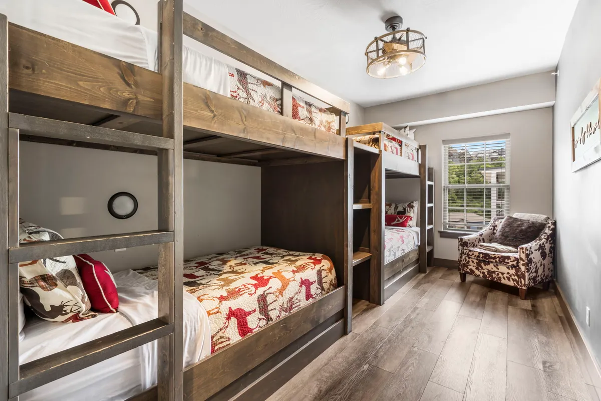 A playful bunk room with built-in bunk beds, a plush chair, and ample natural light pouring in through the window. The beds are designed for fun, sleepovers, and camaraderie, creating a joyful atmosphere for children.