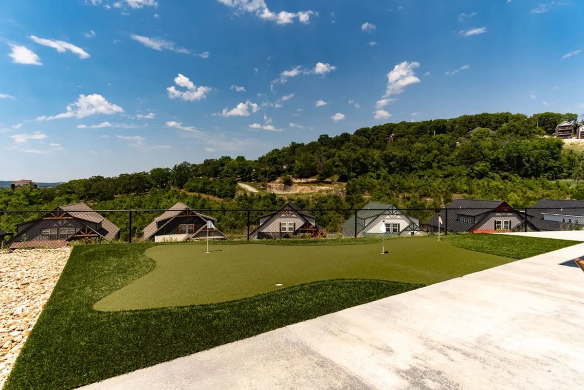 An exterior shot from a broader vantage, showing the putting green framed by serene landscape, distant hills, and nearby houses. The atmosphere is tranquil and leisurely, perfect for unwinding or hosting outdoor games and gatherings.