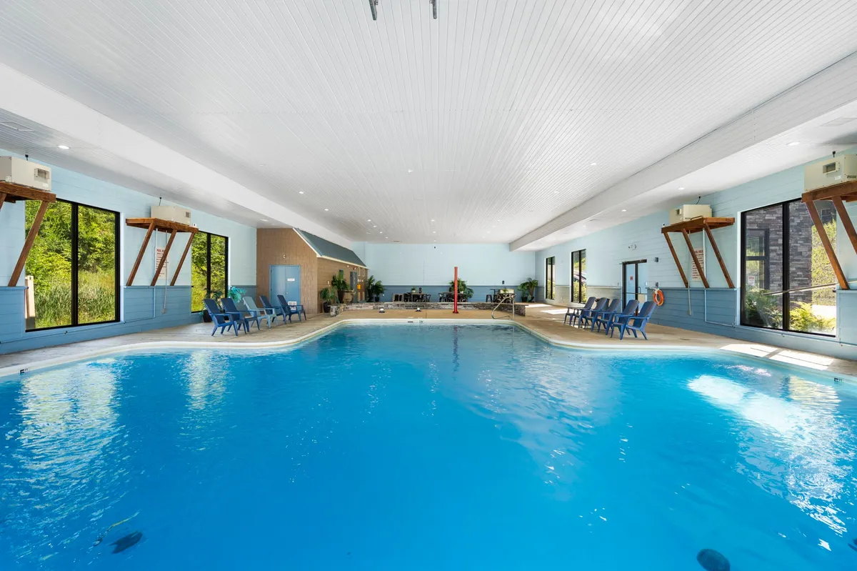 An interior shot of the year-round indoor pool, with large windows allowing natural light to fill the space. Poolside chairs and a lifeguard station indicate a safe and inviting environment for swimming, relaxing, and informal gatherings.