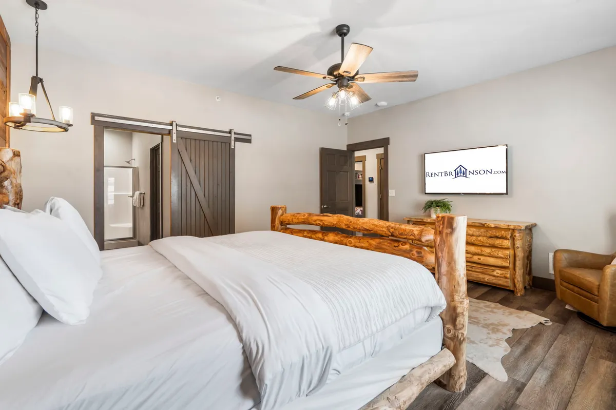 A warmly lit bedroom featuring a log bed, wooden furniture, a TV, and a comfortable chair. Soft natural light streams through the window, highlighting the tranquil and welcoming atmosphere.
