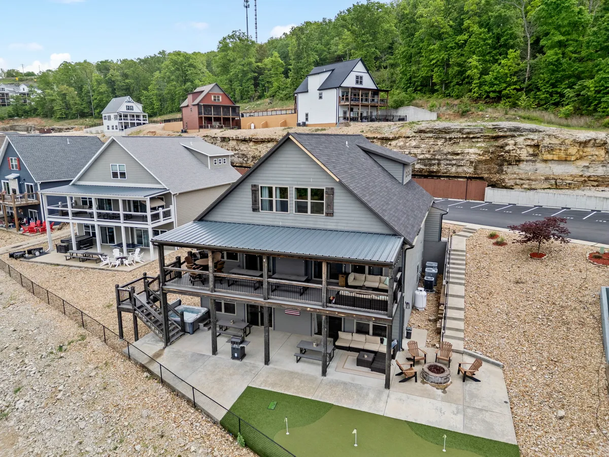 A welcoming exterior shot showcasing the two-story lodge with a covered porch, a cozy fire pit area, manicured lawn, and mature trees. The setting highlights spaces perfect for evening gatherings, story-telling, and relaxing by the fire under the stars.