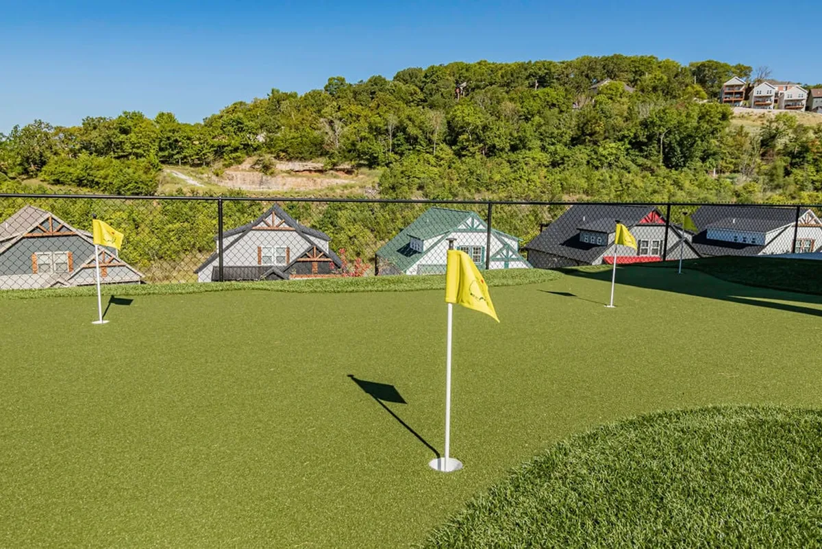 A vibrant exterior image featuring a lush putting green with visible golf flags, surrounded by well-kept lawns and neighboring homes. The setting appears inviting for both golf practice and social gatherings, with a warm, relaxed atmosphere.