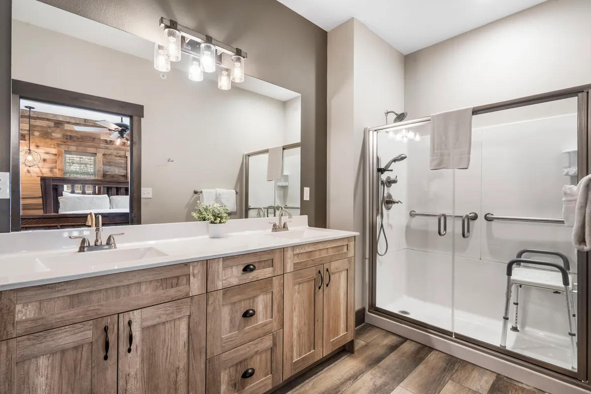 A bright, spa-like bathroom featuring a double sink vanity, framed mirror, modern shower area, and wood accents. The layout is accessible and evokes a sense of calm and rejuvenation.